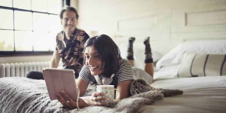 Smiling couple relaxing, drinking coffee and using digital tablet on bed 