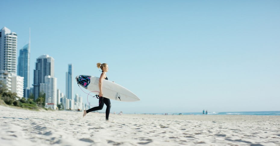 Woman running on beach with surfboard, Gold Coast, Australia. 